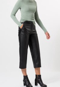 Black leather cropped pants with side pockets, paired with a ribbed, light green long-sleeve top. Black heeled ankle boots complete the outfit.