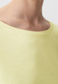 Gul bomullströja med ribbad halsringning, med en mjuk textur och en något lös passform som fångar den övre delen och axelområdet.