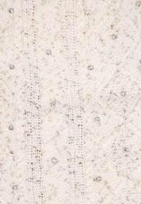 Maglione lavorato a maglia di colore crema chiaro con motivo a trecce, arricchito da piccoli dettagli in argento per aggiungere texture e particolari.