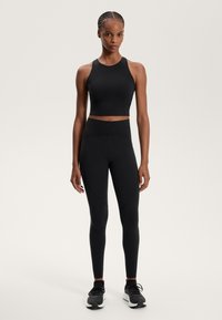 Top sportivo nero e leggings a vita alta realizzati in tessuto elasticizzato con design senza cuciture e dettagli di cucitura sottili. Scarpe sportive nere incluse.