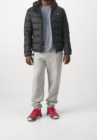 Czarna kurtka puchowa z kapturem, szary t-shirt, szare dresy oraz czerwone buty sportowe z szarymi akcentami, stojący na białym tle.