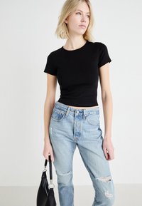 Zwarte cropped t-shirt met korte mouwen, gecombineerd met lichtblauwe distressed jeans; vasthoudend een zwarte handtas, gladde stof, casual pasvorm.