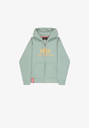 Minttivihreä vetoketjullinen huppari, jossa on etutaskut, nyörillä säädettävä huppu, keltainen "Alpha Industries" -logo ja punainen merkki helmassa.