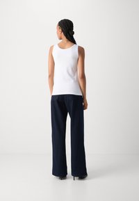White sleeveless top paired with loose-fitting dark navy trousers, made from textured fabric, featuring wide legs and subtle stitching detail.