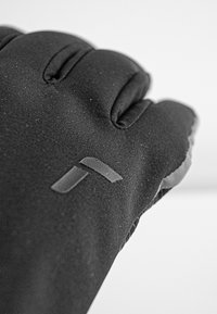 Sort stofhandske med tekstureret overflade, polstrede sektioner og matte stropdetaljer. Har en tætsiddende pasform med definerede fingersektioner.