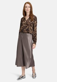 Braun geflecktes Leopardenmuster, langärmlige Bluse, kombiniert mit einem satinartigen, knielangen, taupefarbenen Rock. Das Model trägt silberne Ballerinas mit einem Riemendetail.