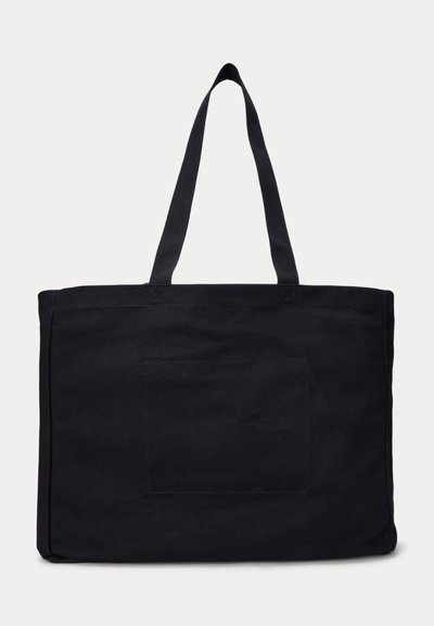 Μεγάλη μαύρη πάνινη τσάντα ώμου με δύο μακριές λαβές και ραμμένη ορθογώνια τσέπη στη μία πλευρά, τοποθετημένη σε λευκό φόντο.