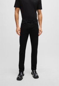 Black denim jeans with a slim fit, five-pocket design, and subtle stitching details, paired with black loafers and a black t-shirt.
