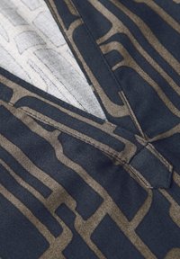 Tessuto navy con un motivo geometrico beige; presenta un design a V e dettagli di cucitura visibili, evidenziando texture e struttura.