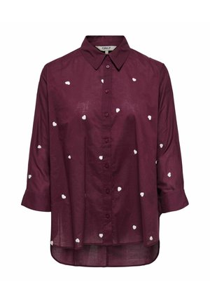 Chemise boutonnée bordeaux avec col, ornée de broderies en forme de cœur blanches sur l'ensemble et de manches longues avec des poignets retroussés.