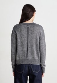 Pull en tricot gris avec un col rond, présentant un détail de couture verticale à l'arrière et des bords côtelés aux poignets et à l'ourlet.