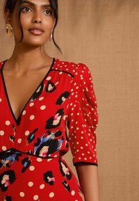 Red dress featuring puff sleeves, a deep V-neck, embellished with black and multicolored leopard spots and white polka dots, outlined in black.