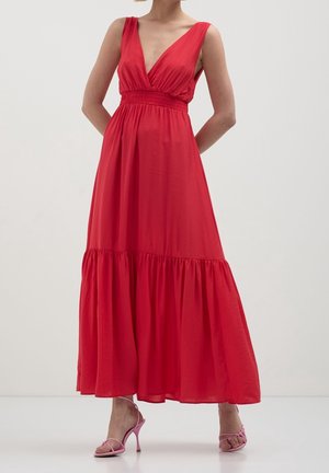 Mujer con un vestido maxi rojo sin mangas con escote en V profundo y cintura fruncida, combinado con sandalias de tacón alto rosas.
