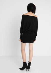 Svart stickad oversized off-shoulder tröja i kombination med en svart figurnära minikjol och högklackade ankelskor, alla med en texturerad finish.