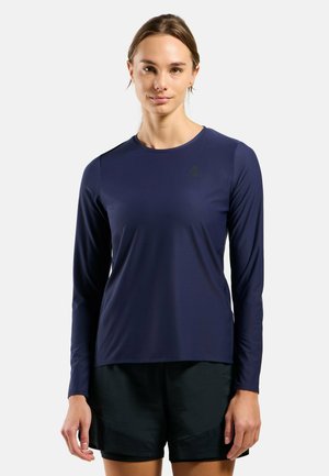 Marinefarbendes, langärmeliges Sportshirt mit rundem Halsausschnitt und glatter Textur, kombiniert mit dunklen Shorts. Es besitzt ein kleines Logo auf der Brust.
