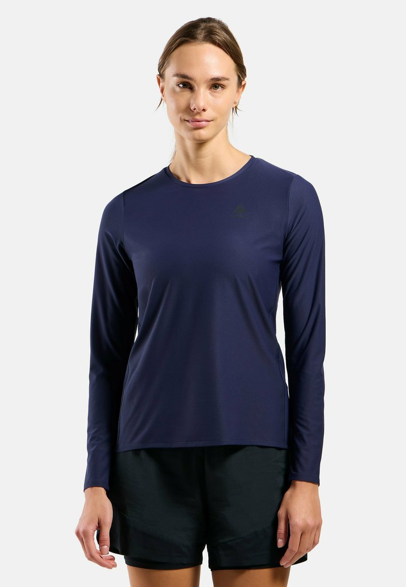 Marinefarbendes, langärmeliges Sportshirt mit rundem Halsausschnitt und glatter Textur, kombiniert mit dunklen Shorts. Es besitzt ein kleines Logo auf der Brust.