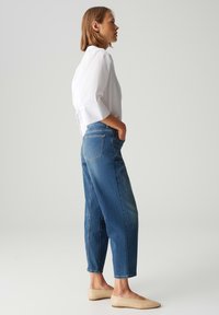 Blusa bianca leggera con maniche a tre quarti, abbinata a jeans blu a vita alta con gamba dritta e ballerine beige. Design semplice.