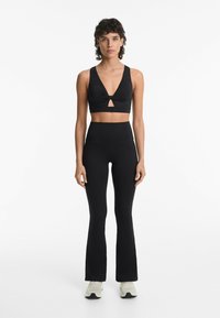 Zwart sportset bestaande uit een cropped tanktop met knoopdetail en keyhole, en high-waisted flared leggings, beide in een gestructureerde stof.
