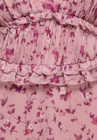 Tissu rose avec un petit imprimé floral violet et blanc, comportant des parties froncées et un bord volanté superposé.