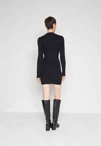 Svart ribbad klänning med lång ärm, i mid-thigh längd. Kombinerad med knähöga svarta stövlar med en kraftig klack för extra höjd.