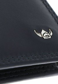 Coin de portefeuille en cuir noir avec une couture détaillée et un petit emblème argenté en forme de casque ailé avec la lettre "G".