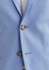 Light blue blazer with a textured fabric, featuring two brown buttons and detailed stitching around the buttonholes.