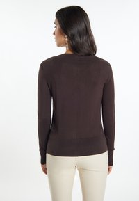 Bruine trui met lange mouwen, aansluitend ontwerp, geribbelde boorden en zoom. Gladde textuur, achterkantnaad detail, gecombineerd met crèmekleurige broeken.