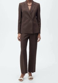 Completo marrone su misura con blazer doppiopetto e pantaloni a gamba dritta. Presenta una texture liscia e linee strutturali sottili. Da abbinare a sandali beige.