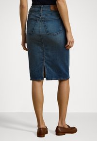 Denim suknja olovka u srednje plavoj boji, s prorezom straga, dva stražnja džepa i kožnim oznakom na struku. Glatka tekstura.