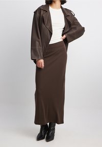 Veste de moto en faux cuir marron sur un haut ajusté blanc, assortie d'une jupe maxi marron et de bottines à talons noires.