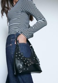 Sort læderhandtaske med blomsterdekorationer og sølvdetaljer, kombineret med en stribet langærmet top og mørke denim jeans.