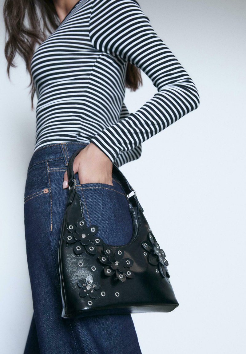 Sort læderhandtaske med blomsterdekorationer og sølvdetaljer, kombineret med en stribet langærmet top og mørke denim jeans.