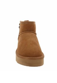 Stivale alla caviglia in suede color tan con punta arrotondata, dettagli cuciti attorno alla parte superiore e suola in gomma marrone chiaro. Presenta un pratico passante laterale.