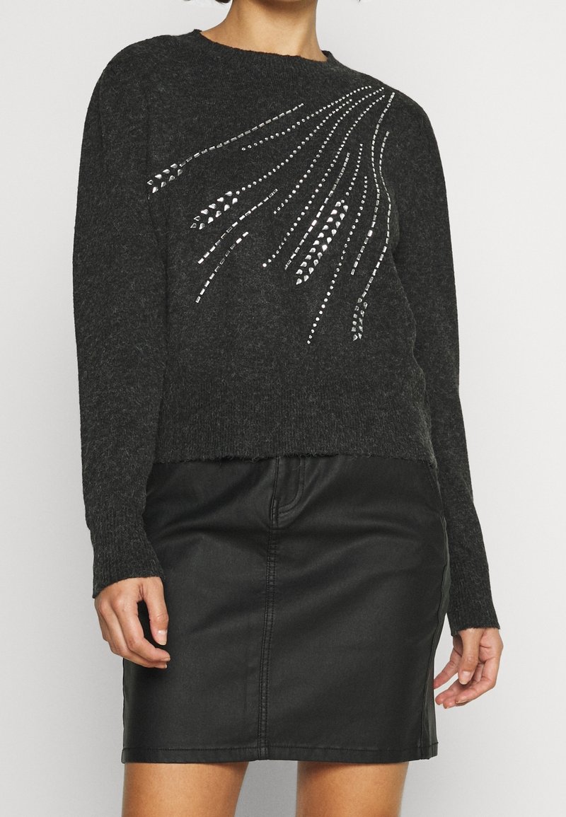 Ciemnoszary dzianinowy sweter z okrągłym dekoltem i błyszczącymi ozdobami w płynnym wzorze. Połączony z czarną skórzaną spódnicą.
