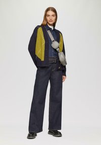 Granatowy kardigan z żółtym wzorem geometrycznym, w połączeniu z dżinsową koszulą i szerokimi ciemnymi dżinsami. Uzupełniony szarym torebką na ramię.