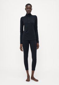 Top negru cu mânecă lungă, cu guler tip quarter-zip, și colanți negri. Ambele sunt ajustate, realizate dintr-un material elastic cu o textură netedă.