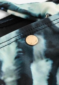 Blå og sort mønstret stof med glat tekstur, prydet med et rundt guldmærke præget med "MINT", der er fastgjort til kanten.