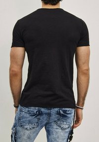 T-shirt noir à manches courtes avec un design ajusté, fabriqué en matériau doux, présenté de dos, associé à un jean en denim bleu.