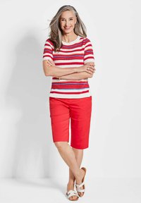 Rood en wit gestreepte korte mouw sweater gecombineerd met rode knielange shorts en witte sandalen. De stof lijkt licht en glad.