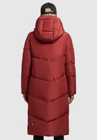 Abrigo largo acolchado rojo con capucha, que presenta patrones en forma de chevrón cosidos y un parche con logotipo en el dobladillo. Textura de tejido suave.