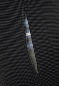 Schwarzer, strukturierten Stoff mit einem vertikalen Schlitz, der ein gestreiftes Muster in Blau, Weiß und Olivgrün im Inneren der Öffnung zeigt.