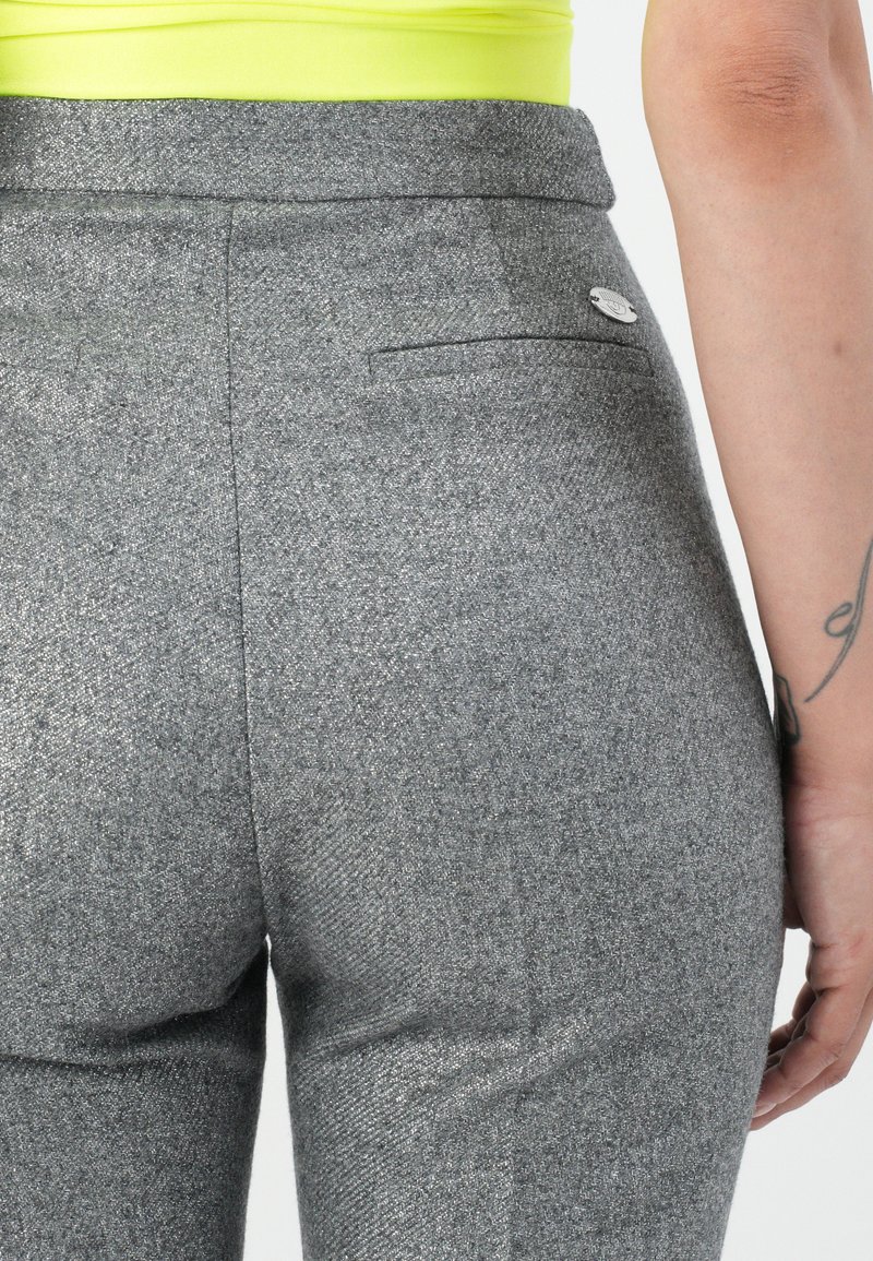 Pantalones grises texturizados con un diseño ajustado, detalle de bolsillo trasero y acento de botón metálico. Combinados con una blusa amarilla brillante.