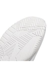 Gros plan de la semelle d'une basket blanche avec des motifs de crampons en zigzag et linéaires pour l'adhérence et la flexibilité.