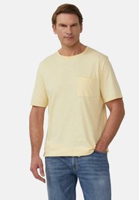 Korte mouwen pastelgele t-shirt met een ronde hals en een borstzak, gemaakt van een zachte, gestructureerde stof. Gedragen met blauwe denim jeans.