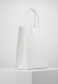 Sac fourre-tout blanc avec un design structuré, logo en relief "TED BAKER LONDON", texture lisse et poignées plates.