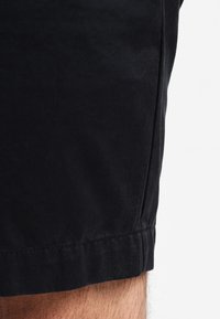 Pantaloni scurți negri din bumbac, cu o textură netedă, cusături ordonate pe margine și un croi drept, oferind un design clasic și simplu.