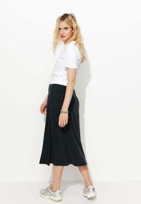 T-shirt blanc associé à une jupe midi fluide noire. La tenue est complétée par des baskets argentées et blanches. Texture de tissu lisse.