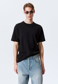 T-shirt noir en coton à manches courtes, col rond, associé à un jean en denim bleu clair, présentant une coupe décontractée et un léger effet vieilli.