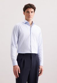 Camicia bianca con motivo a griglia blu, maniche lunghe, colletto abbottonato; abbinata a pantaloni blu navy, con pences e tessuto liscio.