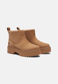 Bottines en suède marron avec une doublure en fourrure douce, une semelle épaisse et des languettes de tirage. Présente un logo d'arbre embossé sur le côté.